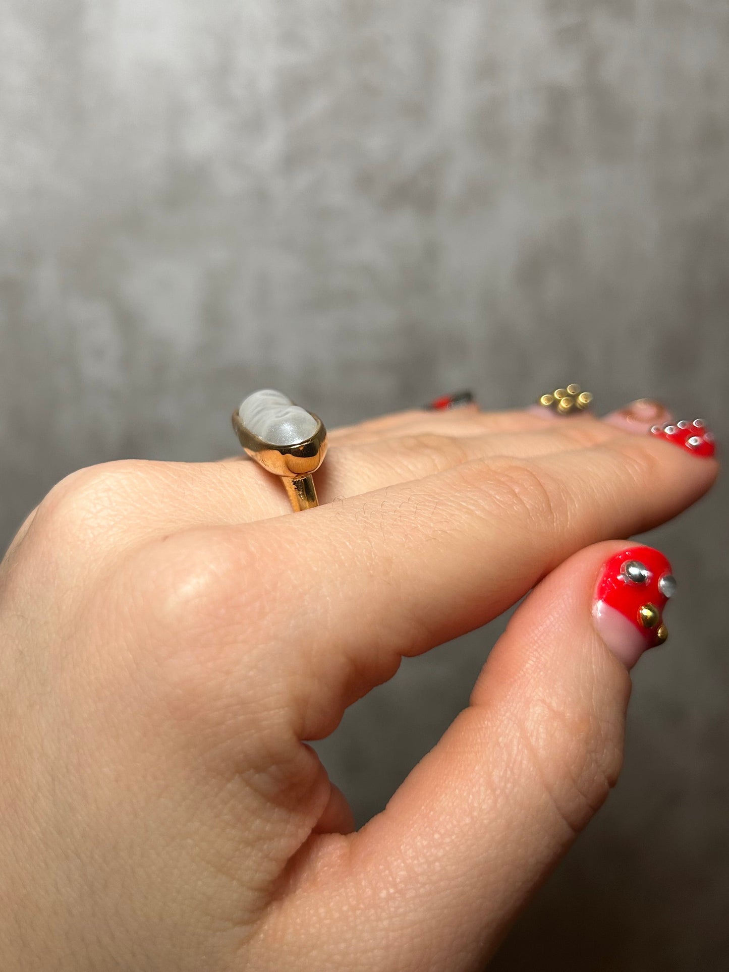 Close-up of a hand wearing a ring with a gray stone on a neutral background
