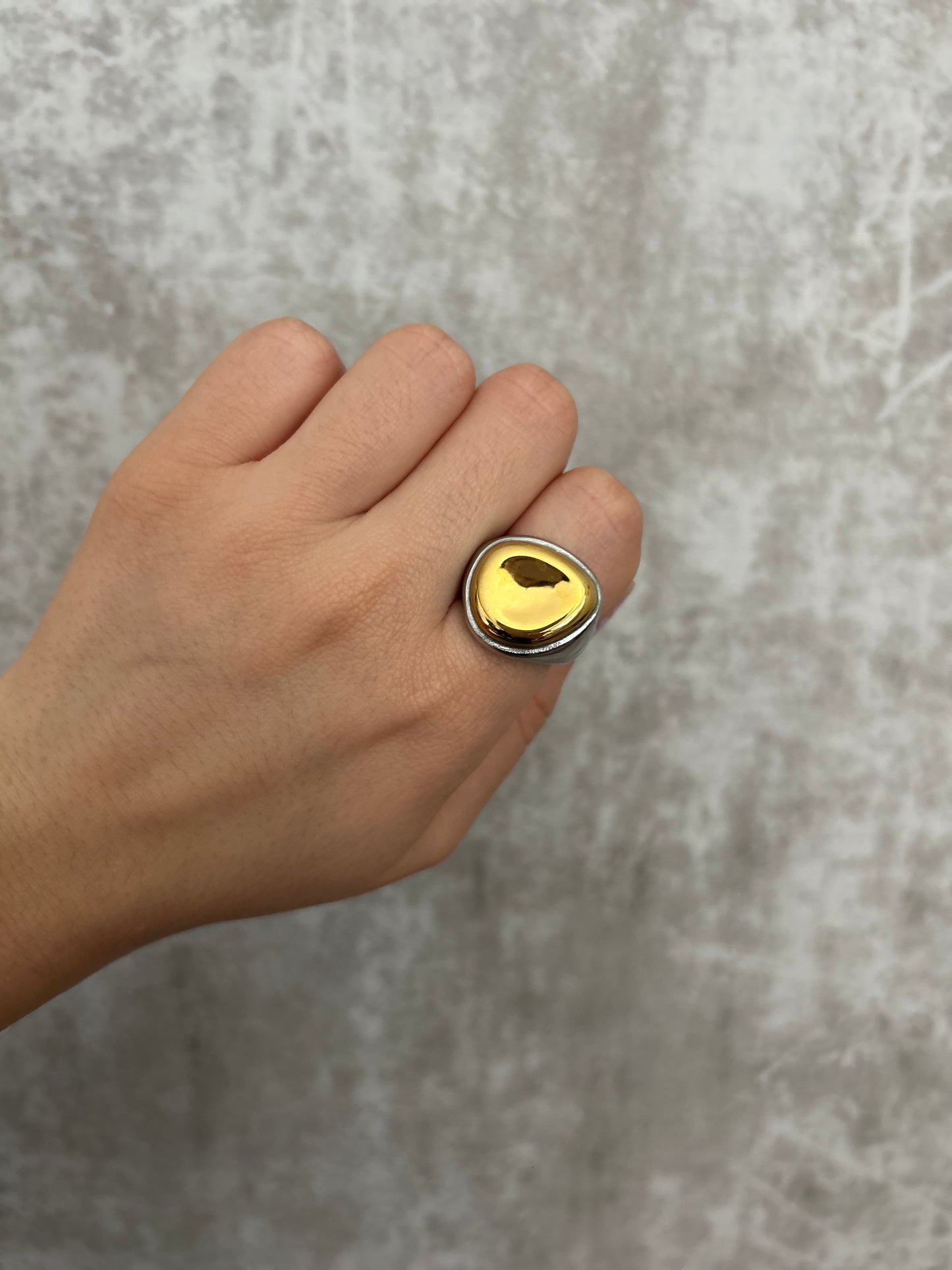 Hand wearing a gold ring on a gray background