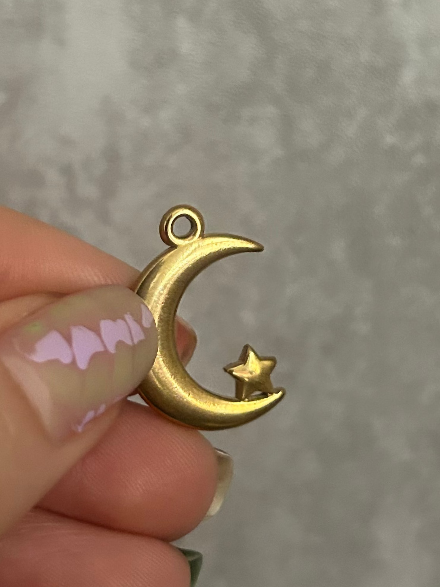 Gold crescent moon and star pendant held by a hand against a gray marble background