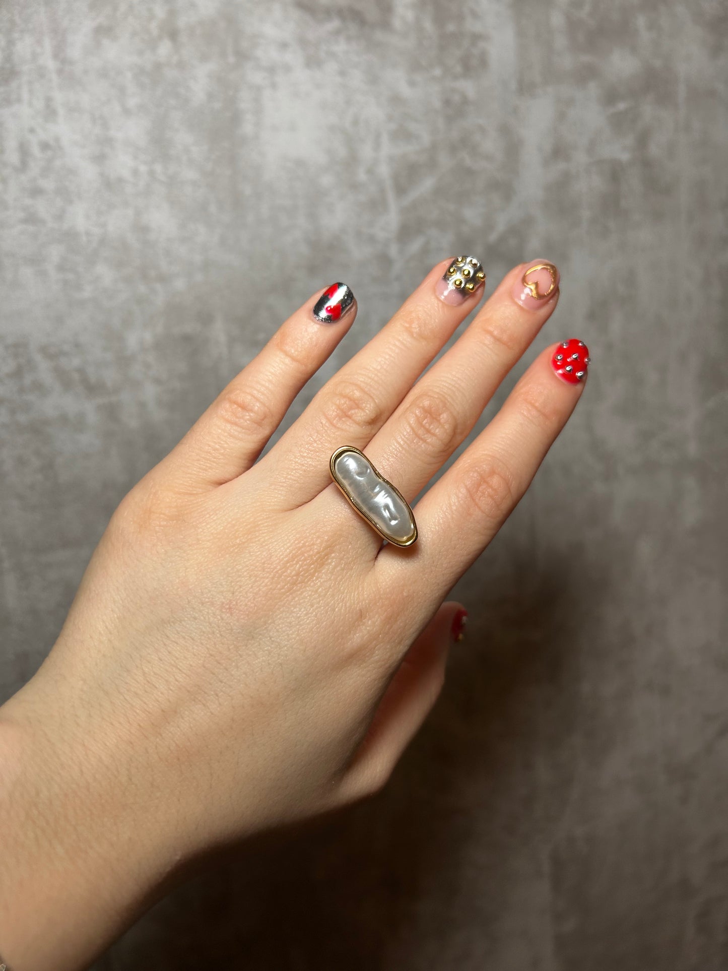 Hand wearing a ring with a pearl-like stone on a gray background