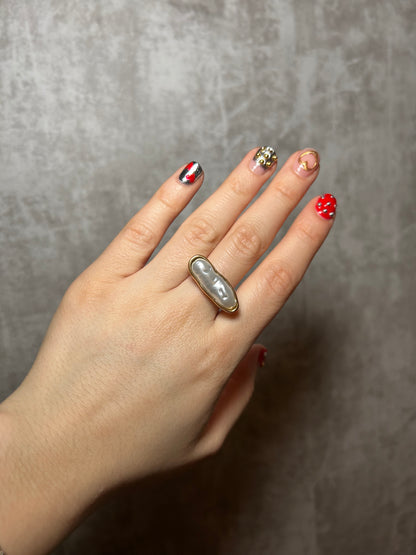 Hand wearing a ring with a pearl-like stone on a gray background