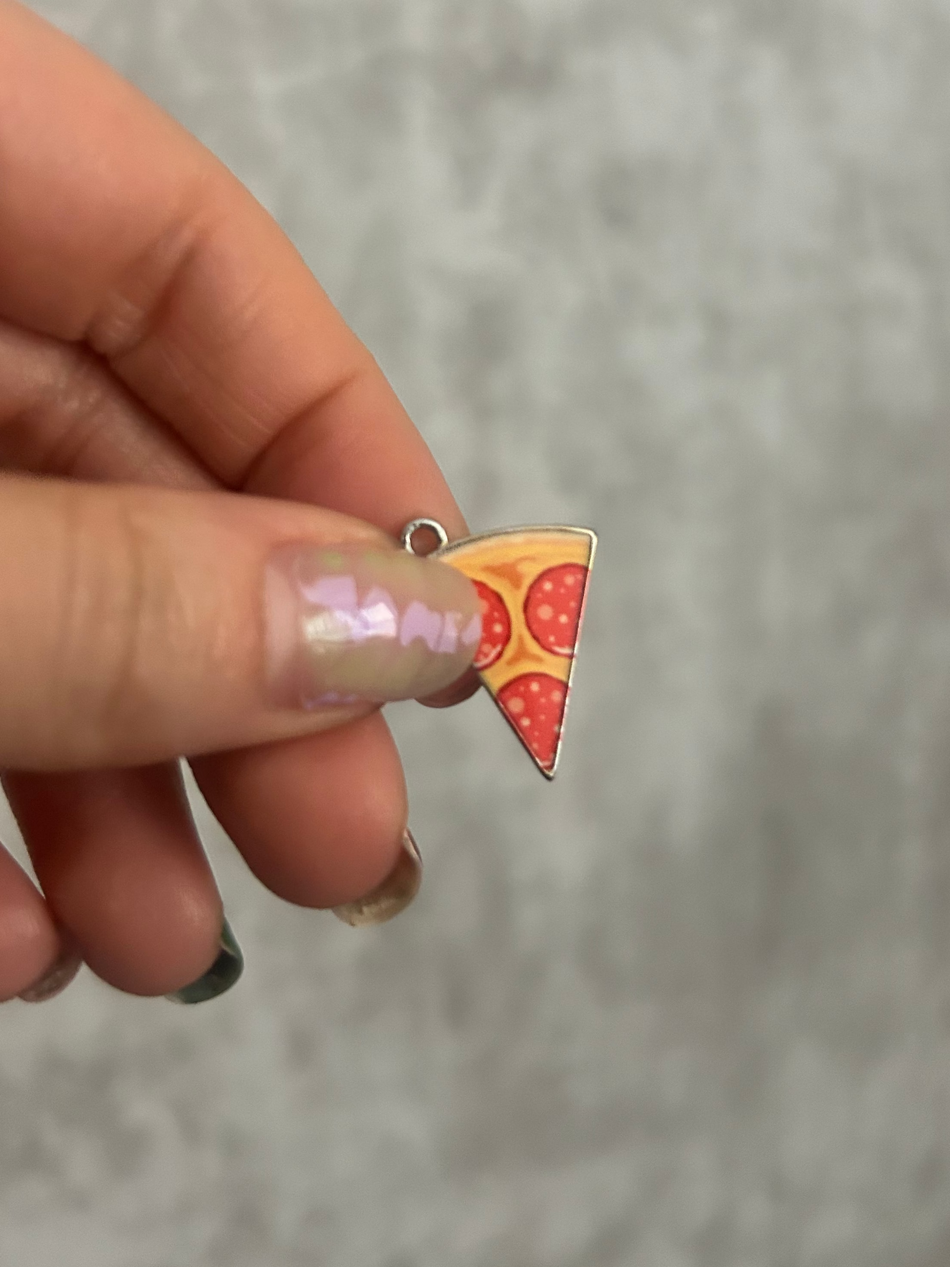 Hand holding a pizza slice-shaped charm against a gray background