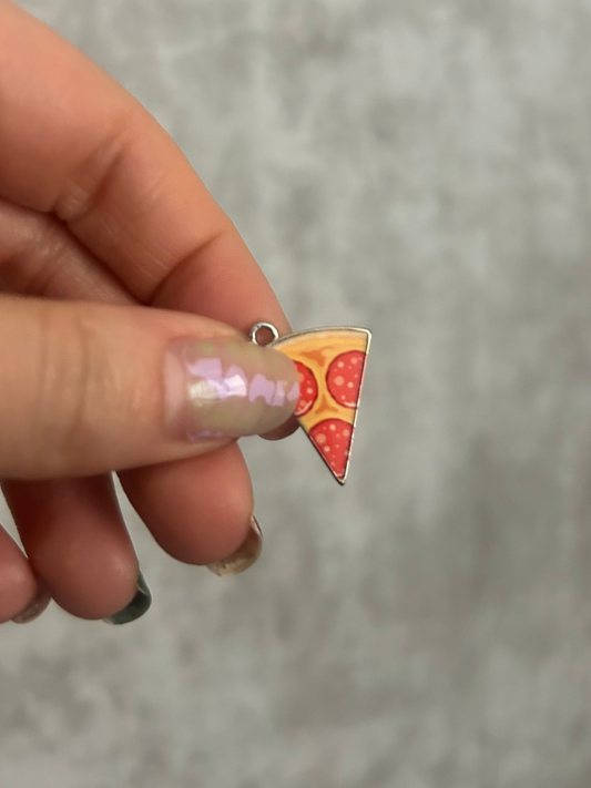 Hand holding a pizza slice-shaped charm against a gray background
