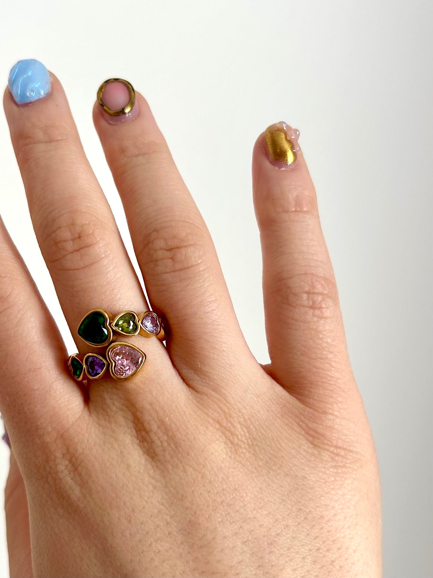 Hand modeling rainbow heart ring in sunlight – colorful reflective stones