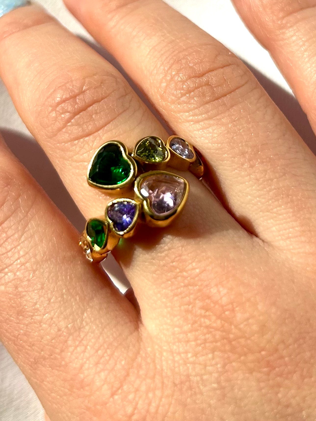 Model wearing gold adjustable rainbow heart ring on hand with natural nails