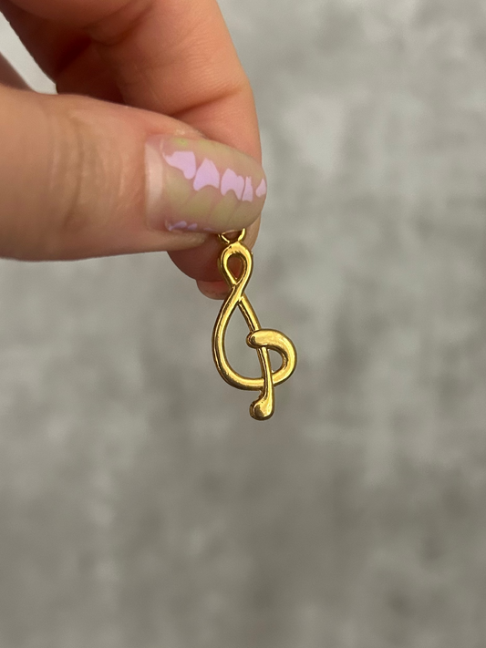 Gold treble clef earring held between fingers against a gray background