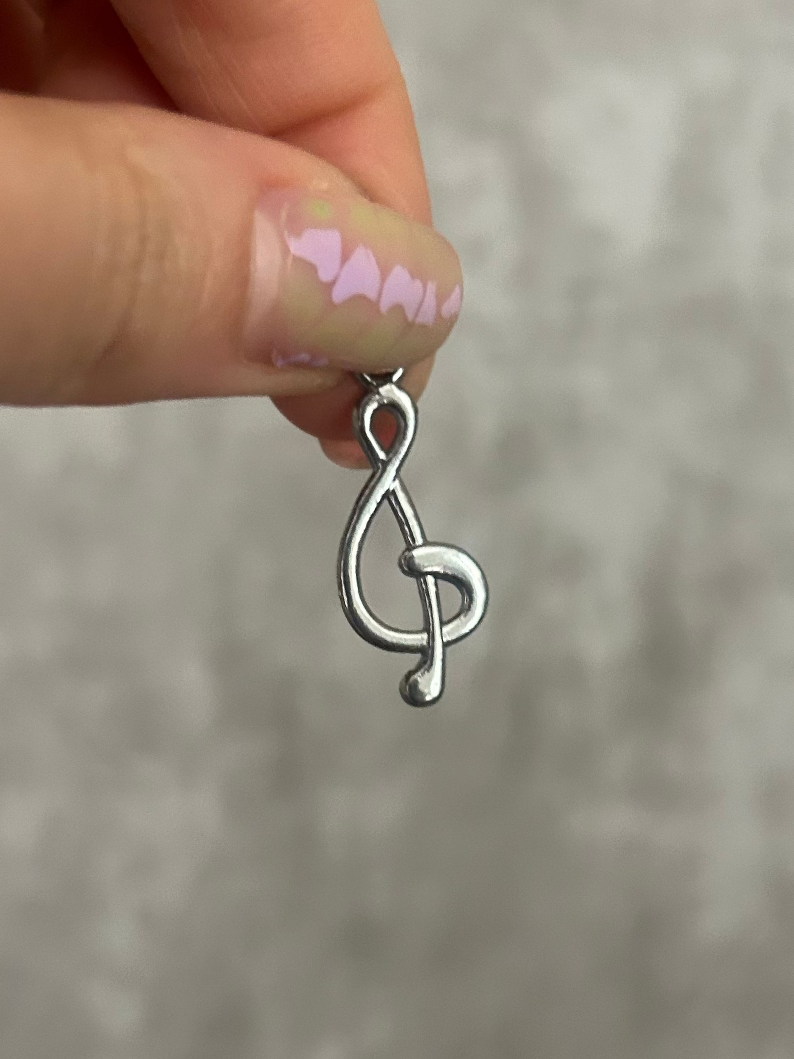 Silver music note charm held by a hand against a gray background