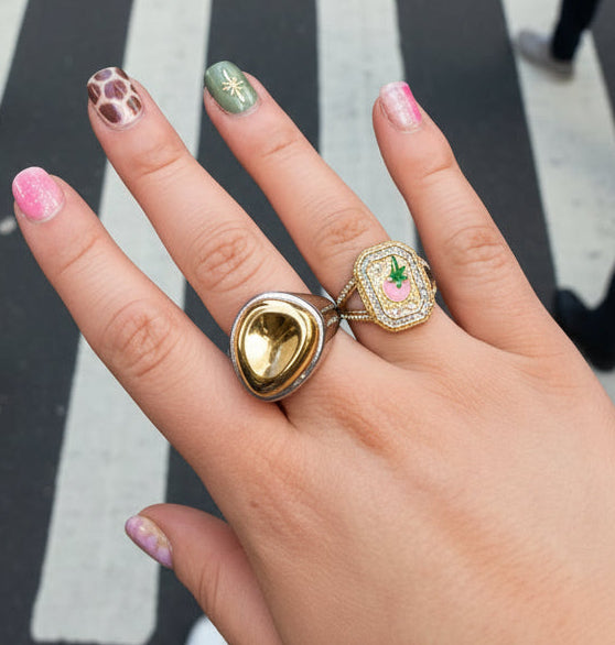 Hand wearing two gold rings with decorative stones on a blurred background